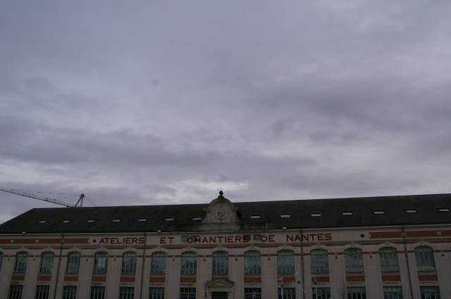 Image illustrant l'article. Photo des Ateliers et chantiers de Nantes sur le parc des Chantiers. Le ciel gris prend la moitié haute de la photo.